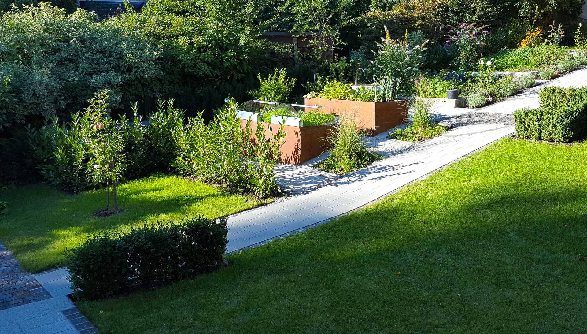 Moderner Garten mit Hochbeeten, gepflastertem Weg und vielfältiger Bepflanzung Garten mit grünen Hochbeeten aus Holz, gepflegtem Rasen, Sträuchern und bepflastertem Gehweg